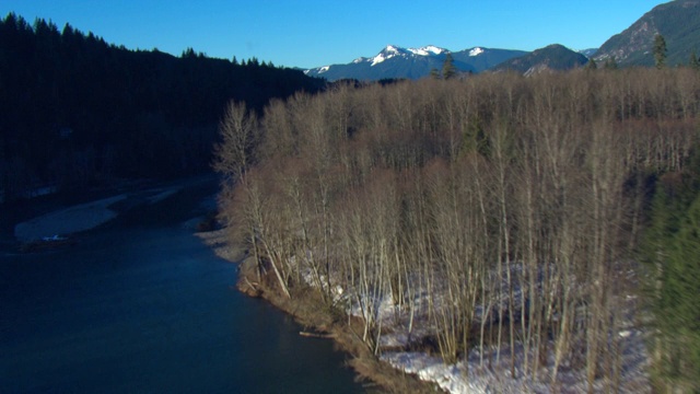 一条河流穿过一个山谷，山谷边点缀着积雪和森林。视频素材