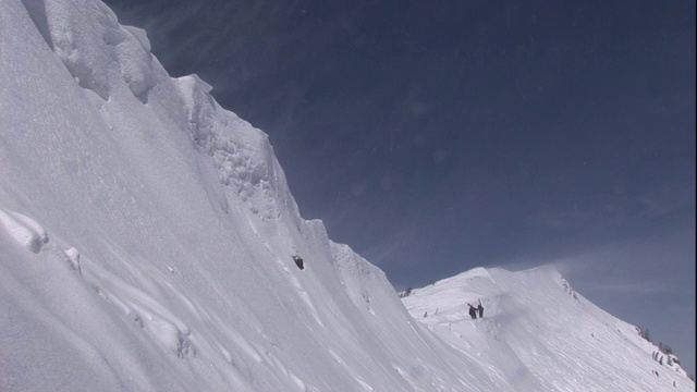 两个人走在一座山上容易发生雪崩的雪帽上视频素材