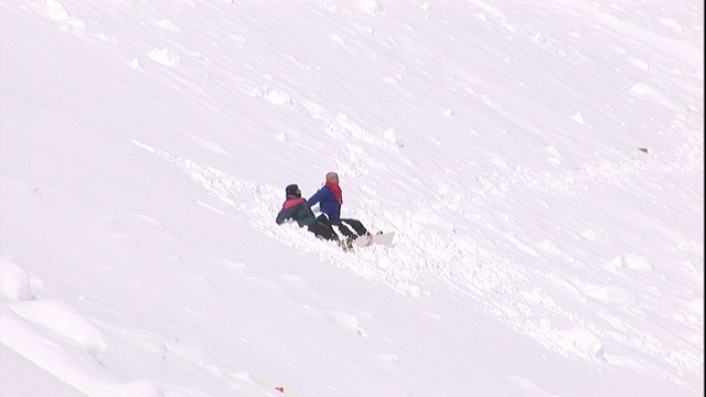 两个穿着冬装的人体模型坐在一个积雪的山坡上。视频素材