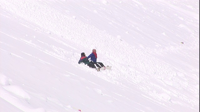 山上有两个穿着冬装的人体模型，一阵小雪崩从他们身边滑过。视频素材