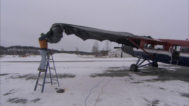 当飞行员从一架小型飞机上取下机翼盖时，地面上覆盖着积雪。视频素材