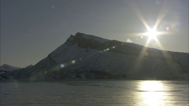 阳光在冰雪覆盖的海岸山下的峡湾上闪烁。视频素材