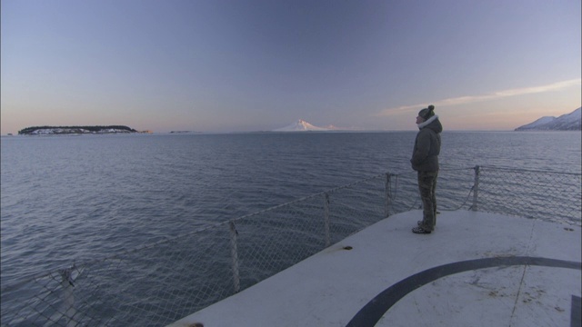 一个旅行者在一艘探险船上的直升机停机坪上注视着荒野的海岸线。视频素材