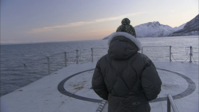 一个旅行者从一艘探险船的直升机停机坪上看着白雪覆盖的火山。视频素材