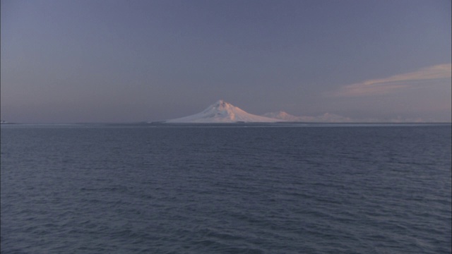 一名游轮乘客看着荒野海岸上白雪覆盖的火山。视频素材