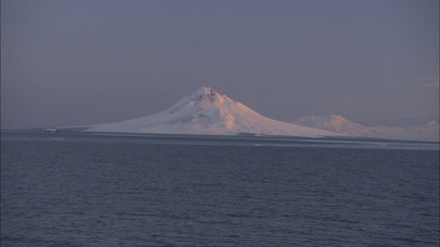 一座白雪覆盖的火山耸立在荒野峡湾的海岸线上。视频素材