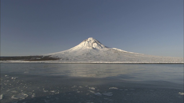 一座白雪覆盖的火山倒映在附近峡湾的水中。视频素材