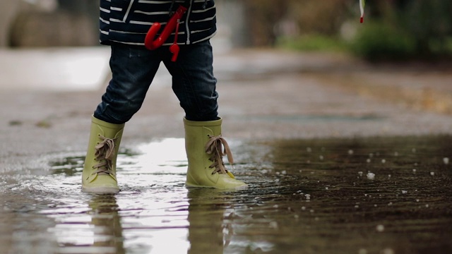 小男孩穿着胶靴在雨中走过水坑视频素材