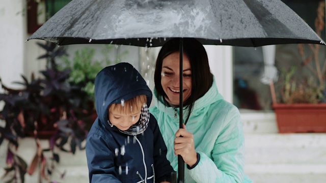 年轻的母亲和她的儿子躲在雨伞下下雨视频素材