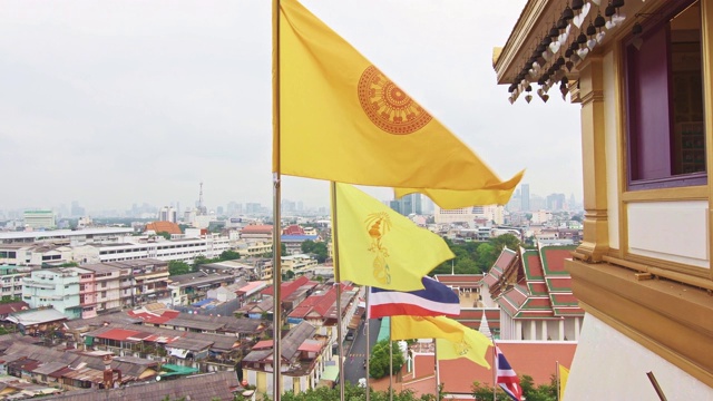 泰国曼谷，金山寺附近，旗帜在风中飘扬。泰国国旗与佛教旗帜靠近楼梯到寺庙的顶部。在遥远的曼谷的城市景观视频素材