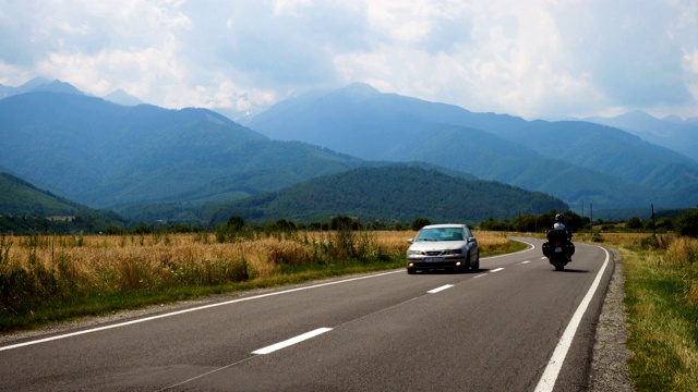 在阳光明媚的夏日，汽车行驶在通往远处山区的道路上视频素材