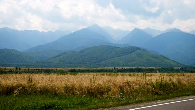 在阳光明媚的夏日，汽车行驶在通往远处山区的道路上视频素材