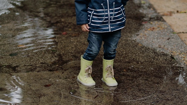 小男孩穿着胶靴在雨中走过水坑视频素材