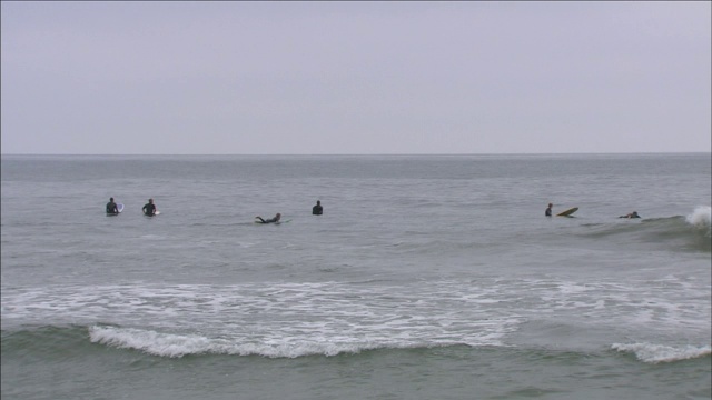 当其他冲浪者浮在他们的冲浪板上时，一个冲浪者抓住了一个小波浪。视频素材