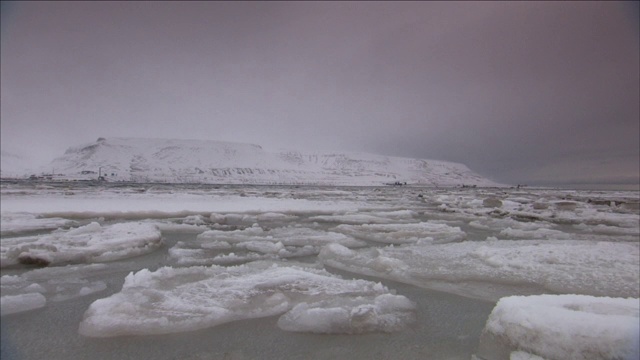 湖面上漂浮着冰，周围是白雪皑皑的山脉。视频素材