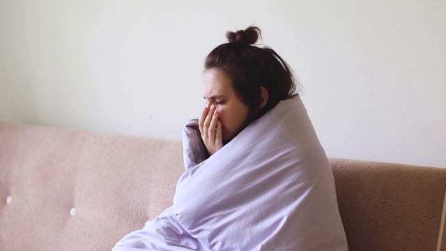 生病的年轻女子因喉咙痛而坐在家里咳嗽。视频素材