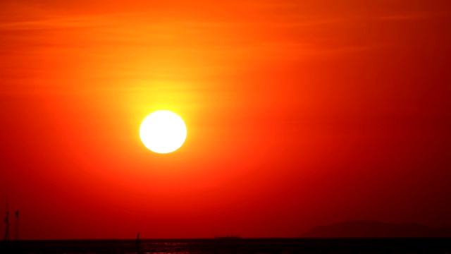 夕阳下，红彤彤的天空落在漆黑的海面上，渔船在流逝视频素材