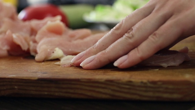 近距离的年轻女子的手切鸡肉在木制砧板在厨房视频素材