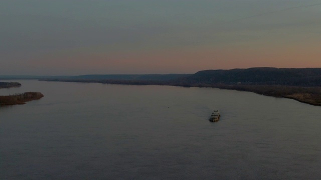 美丽的橙色夜景从无人机河边和森林高地。鸟瞰图上的货船漂浮在海上，在傍晚彩色的天空。岸边的小湖。视频素材