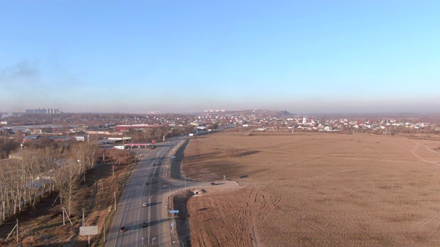 汽车行驶在郊区公路上，沿着秋天的耕地。从农村到城市的公路上鸟瞰经过农田的车辆。全景城市从无人机视频素材