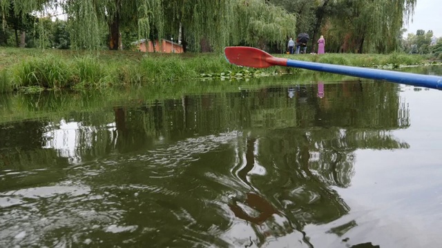 桨在水中。公园里的塑料桨的特写，以湖泊和睡莲为背景。蓝色的塑料桨在水面上划动。红色和蓝色的桨靠近了。水滴往下流视频素材