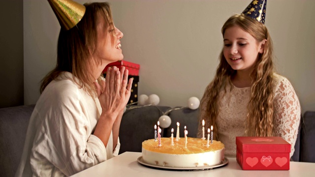 美丽的母亲和她十几岁的女儿正在庆祝生日。妈妈和孩子在吹蛋糕上的蜡烛视频素材