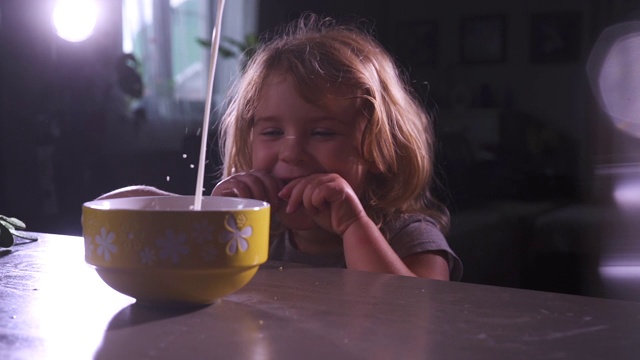 可爱的小女孩笑了，当看到牛奶倒在一碗黄色的玉米片在厨房。快乐有趣的娃娃脸。健康的宝宝的食物。儿童营养。午餐或晚餐，早餐在家吃。视频素材