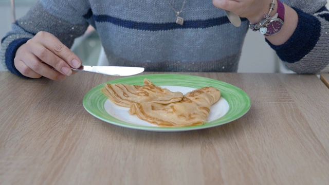 特写:盘子上有两个薄煎饼，女性白种人的手用刀叉切视频素材