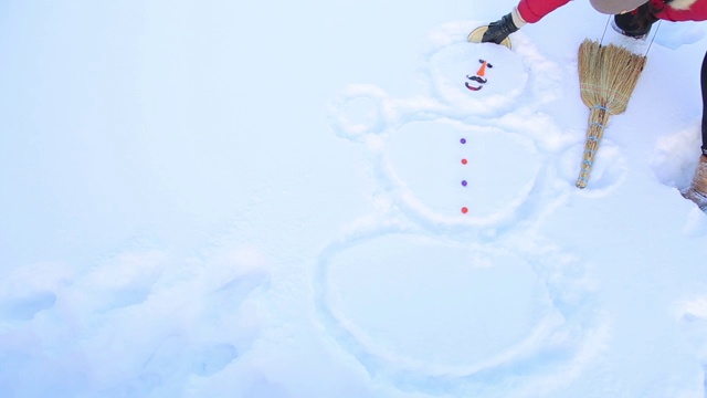 一个女孩在雪地里画了一个雪人，并把一个盖子盖在他的头上视频素材