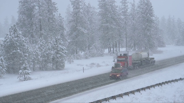 货运卡车在暴风雪中拖着集装箱沿着乡村公路行驶。视频素材