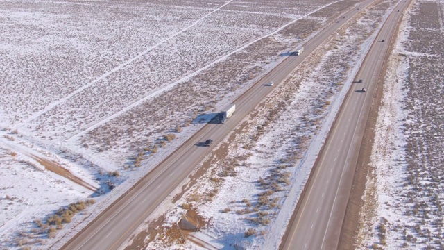 空中飞行在高速公路上，两辆白色卡车在沙漠里运送货物视频素材