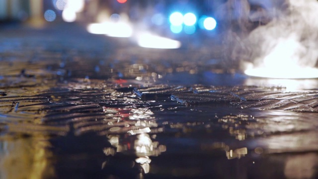 雨点落在城市街道上的慢动作特写，地面灯光在夜晚视频素材