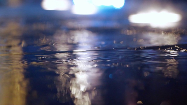 雨点落在水坑上，灯光反射在城市的人行道上视频素材