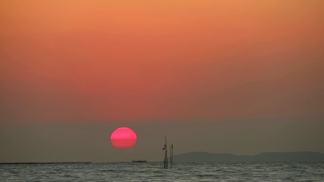 夕阳下，红彤彤的天空落在海面上的云和渔船上，时光流逝视频素材