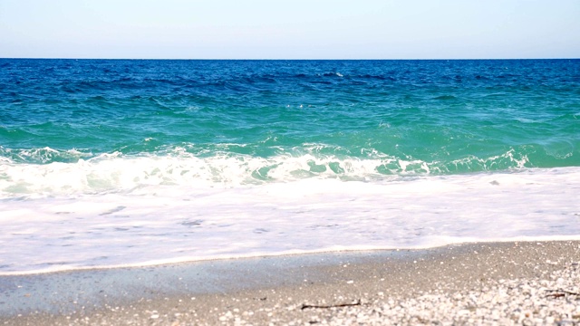 在蓝绿色的海水里，有两个人在游泳。夏天炎热的晴天。海浪在海上，在沙滩上。带着白色泡沫的波浪被冲上岸视频素材