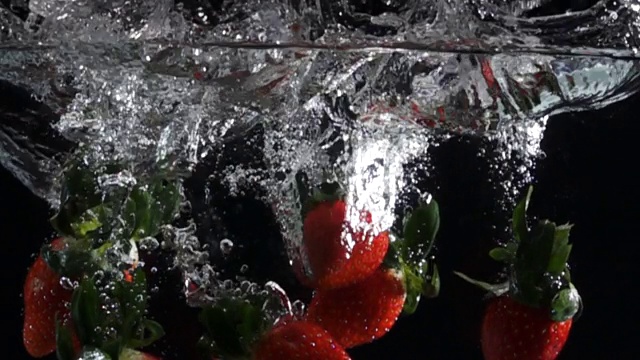 超级慢动作:草莓滴入淡水在黑色的背景视频素材