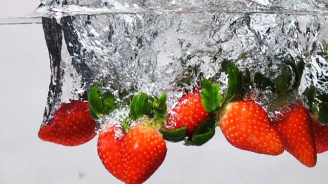 超级慢动作:草莓滴入淡水在白色的背景视频素材