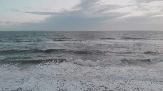 在暴风雨的灰色天空下，海浪在海滩上的冲击镜头通过一个岩石的防波堤(防波堤)视频素材