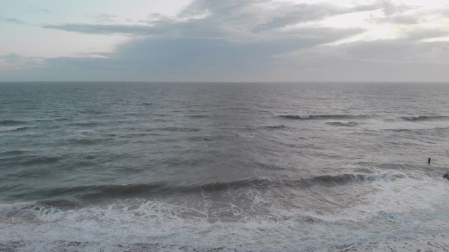 在暴风雨的灰色天空下，海浪在海滩上的冲击镜头通过一个岩石的防波堤(防波堤)视频素材