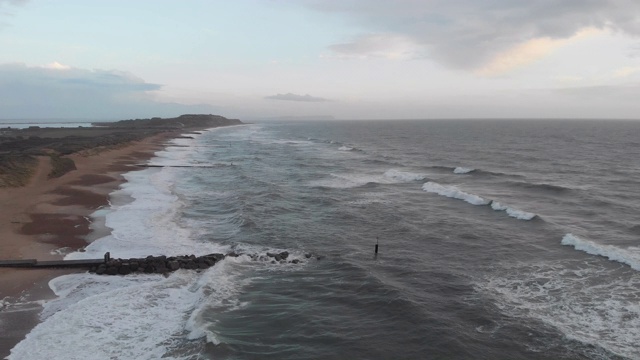 在暴风雨的灰色天空下，海浪在海滩上的冲击镜头通过一个岩石的防波堤(防波堤)视频素材