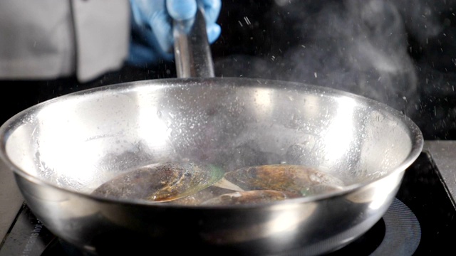 精彩的慢动作食物视频。厨师烹饪或在煎锅中翻炒海鲜。溅油。高清视频素材