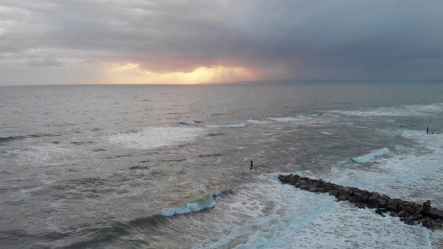 一个空中向后的镜头在一个暴风雨的灰色天空下，在波涛汹涌的海面上的海浪与太阳在云后面发光视频素材