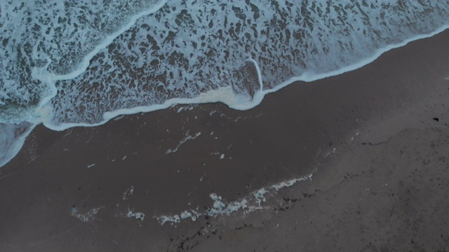 一幅航拍展示了在暴风雨的灰色天空下，海浪在波涛汹涌的海面上撞击的镜头，太阳在云层后面发光视频素材