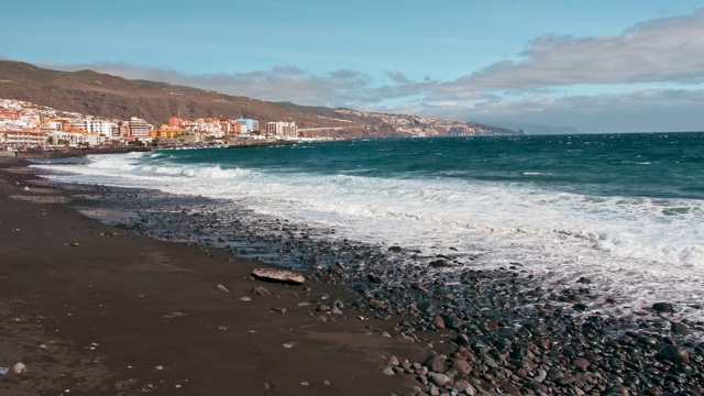 海上冲浪。海岸，碧绿的海浪和白色的泡沫。雨滴飞入相机，火山黑色的石头和沙子海岸。从远处的房屋和旅馆到海边定居视频素材