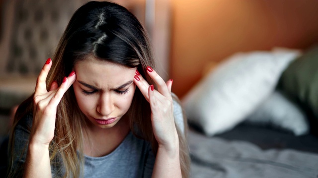 特写压抑的女人按摩太阳穴感觉头痛坐在床上的卧室视频素材