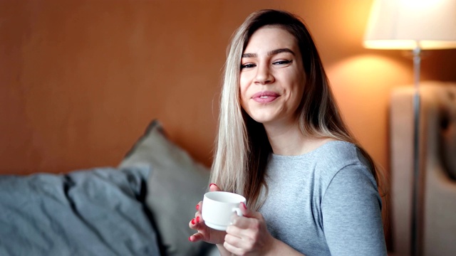 美丽的混血金发女孩的肖像与一杯热茶在舒适的卧室摆姿势视频素材