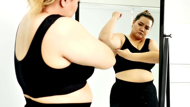 身材高大的年轻女子在运动服看着她的肚子对着镜子视频素材