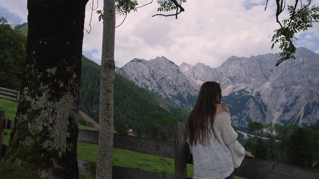 一位女旅行者走在阿尔卑斯山草地的篱笆附近，望着群山视频素材