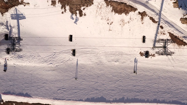 从无人驾驶滑雪电梯在山上度假村移动的俯视图。鸟瞰图滑雪缆车运送滑雪者和滑雪板滑雪者到滑雪场的雪坡上。冬季运动及活动视频素材