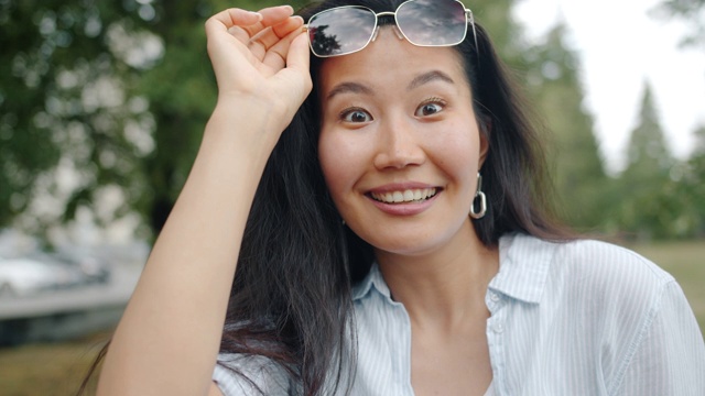 一名亚洲女子在公园里举起眼镜看着镜头大笑的慢镜头视频素材